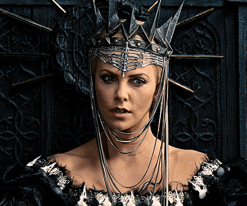 A Woman Wearing A Crown And A Black Dress Looks At The Camera GIF