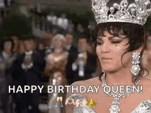 A Woman Wearing A Crown And A Necklace Is Standing In Front Of A Crowd Of People . GIF