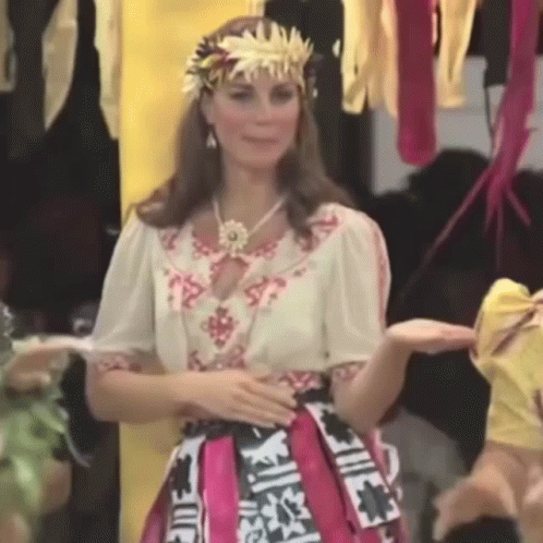 A Woman Wearing A Crown And A Pink Skirt Is Standing In Front Of A Group Of People . GIF