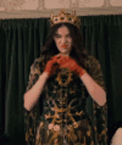 A Woman Wearing A Crown And Red Gloves Is Standing In Front Of A Curtain . GIF