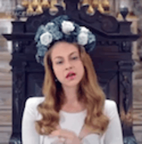 A Woman Wearing A Crown Of Flowers On Her Head Is Sitting In Front Of A Fireplace . GIF