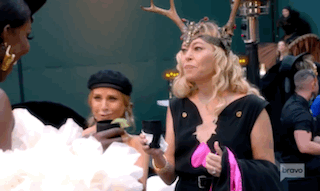 A Woman Wearing A Deer Headband Is Standing Next To Another Woman Holding A Cell Phone . GIF