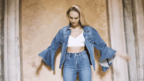 A Woman Wearing A Denim Jacket And Jeans Is Dancing GIF