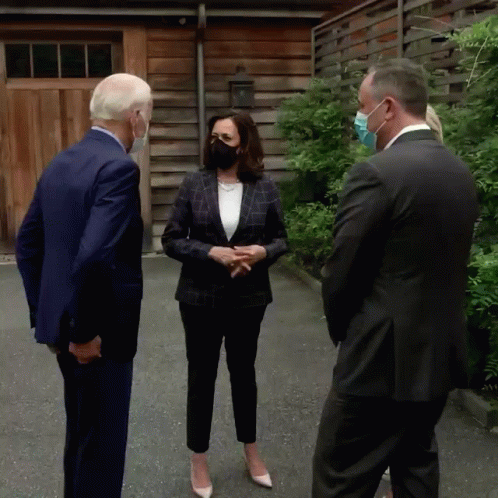 a woman wearing a face mask talks to two men in suits