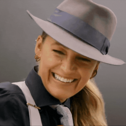 A Woman Wearing A Fedora Hat And Suspenders Smiles GIF