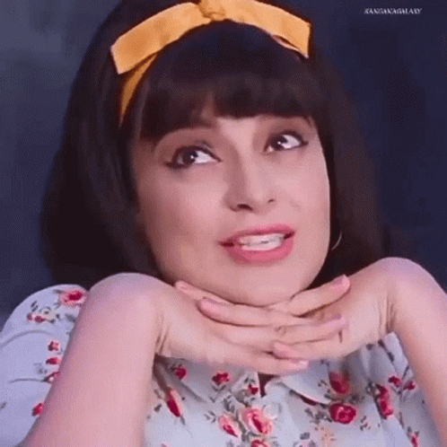 A Woman Wearing A Floral Shirt And A Yellow Headband Is Making A Funny Face With Her Hands On Her Chin . GIF