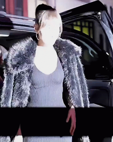 A Woman Wearing A Fur Coat Is Standing In Front Of A Car GIF