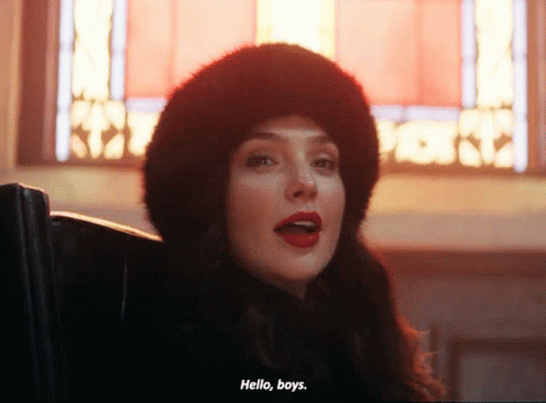 A Woman Wearing A Fur Hat Says Hello Boys In Front Of A Stained Glass Window GIF