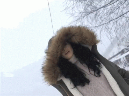 A Woman Wearing A Fur Hooded Jacket Is Standing In The Snow GIF