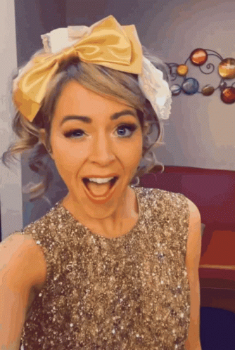 A Woman Wearing A Gold Sequined Dress And A Yellow Bow In Her Hair GIF
