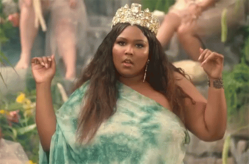 A Woman Wearing A Green Dress And A Crown Is Standing In A Forest . GIF