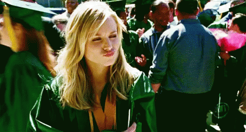 A Woman Wearing A Green Graduation Cap And Gown Is Blowing A Kiss GIF