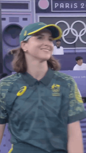 A Woman Wearing A Green Shirt And A Hat Is Smiling In Front Of A Paris Sign GIF