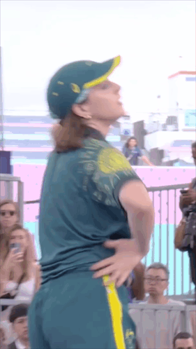 A Woman Wearing A Green Shirt And A Yellow Hat Is Standing With Her Hands On Her Hips GIF