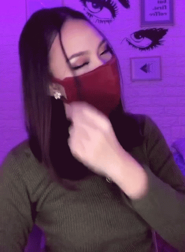 A Woman Wearing A Green Sweater And A Red Mask With A Purple Background GIF