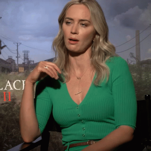 A Woman Wearing A Green Sweater Is Sitting In Front Of A Sign That Says Laci Ii GIF