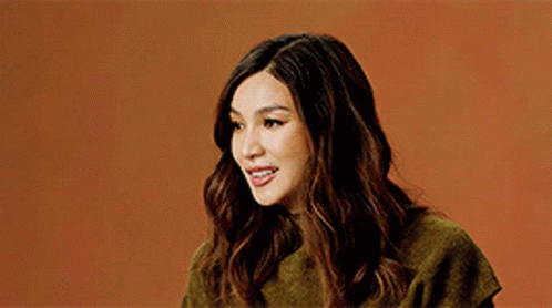 A Woman Wearing A Green Sweater Is Smiling Against An Orange Background . GIF