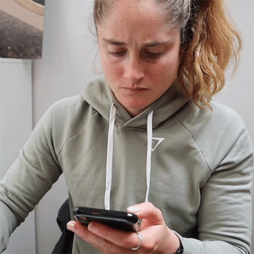 a woman wearing a grey hoodie is looking at her cell phone