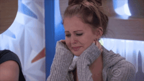 A Woman Wearing A Grey Sweater Is Crying And Covering Her Face With Her Hands GIF