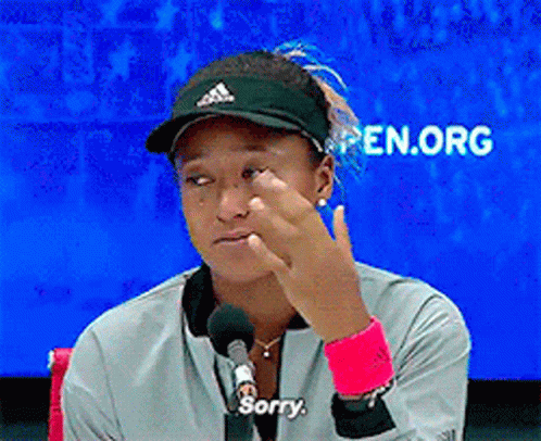 A Woman Wearing A Hat And A Jacket Says Sorry In Front Of A Microphone GIF