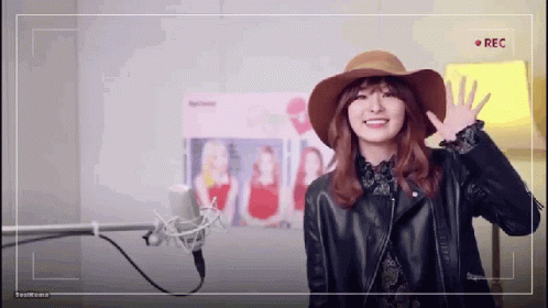 A Woman Wearing A Hat And A Leather Jacket Is Standing In Front Of A Microphone . GIF
