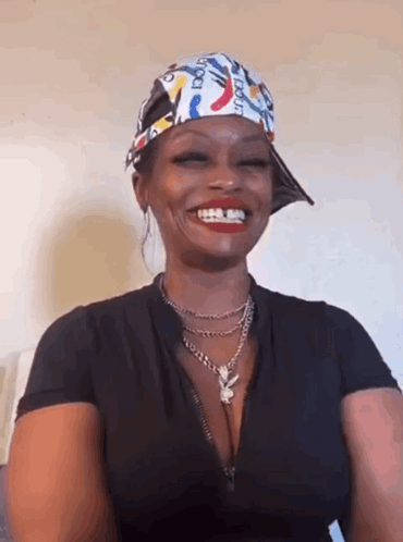 a woman wearing a hat and a necklace is smiling and wearing a bandana .