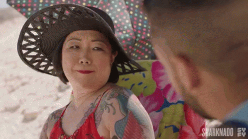 A Woman Wearing A Hat And A Red Bikini Is Sitting On A Beach Chair Looking At A Man . GIF