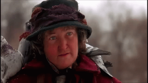 A Woman Wearing A Hat And A Red Coat Is Standing In The Snow GIF