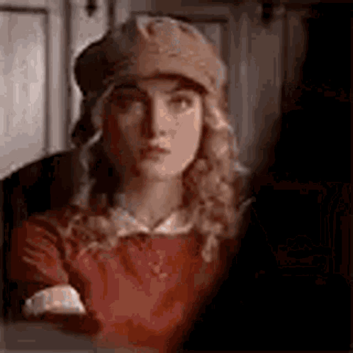 A Woman Wearing A Hat And A Red Shirt Is Looking At The Camera . GIF