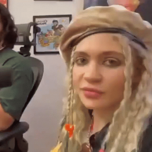 A Woman Wearing A Hat And Braids Is Sitting In A Chair In Front Of A Microphone . GIF