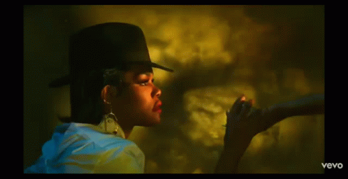 A Woman Wearing A Hat And Earrings Is Smoking A Cigarette In A Vevo Video GIF