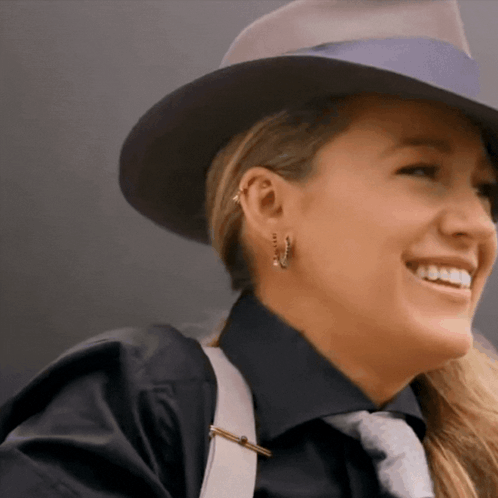 A Woman Wearing A Hat And Earrings Smiles For The Camera GIF