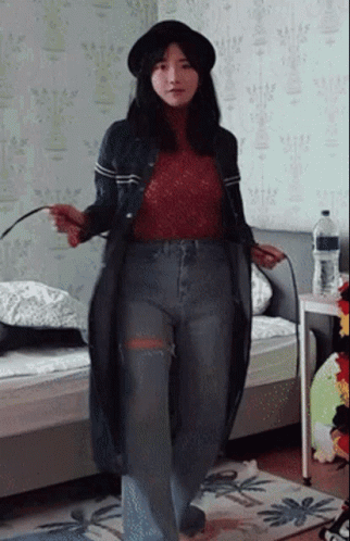 A Woman Wearing A Hat And Jeans Is Standing In A Room GIF