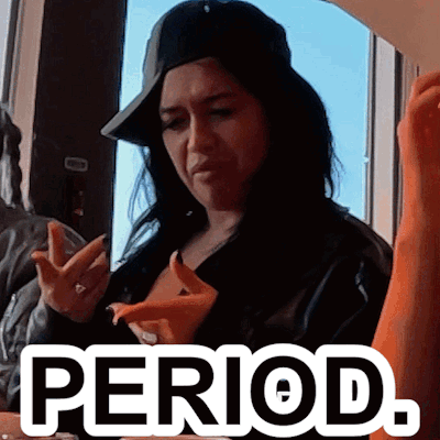 A Woman Wearing A Hat Is Sitting At A Table With The Word Period Written On It GIF