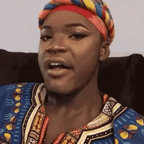 A Woman Wearing A Head Scarf And A Colorful Shirt Is Sitting In A Chair . GIF