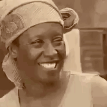A Woman Wearing A Head Scarf And A Hat Is Smiling . GIF