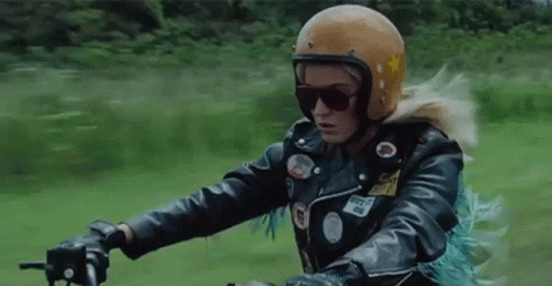 A Woman Wearing A Helmet And Sunglasses Is Riding A Motorcycle On A Road . GIF