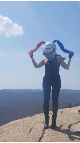 A Woman Wearing A Helmet With A Skull On It Stands On A Rock GIF