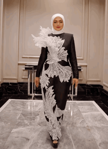 A Woman Wearing A Hijab And A Black And White Dress Is Standing In A Hallway GIF