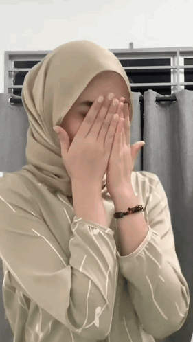A Woman Wearing A Hijab And A Bracelet Covers Her Face With Her Hands GIF