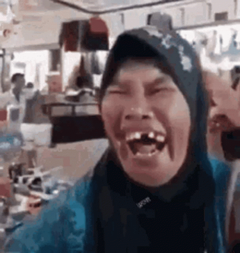 A Woman Wearing A Hijab Is Laughing With Her Mouth Open In A Restaurant . GIF