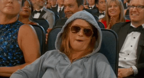 A Woman Wearing A Hoodie And Sunglasses Is Sitting In A Crowd Of People At A Movie Theater . GIF