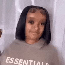 a woman wearing a hoodie with the word essentials on it is looking at the camera .