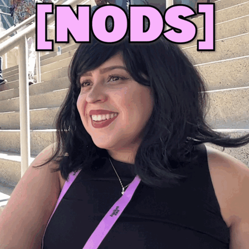 a woman wearing a lanyard that says victoria 's secret smiles in front of stairs