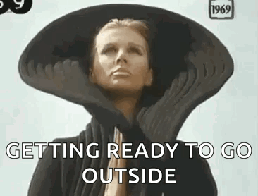 A Woman Wearing A Large Hat And Gloves Is Getting Ready To Go Outside . GIF