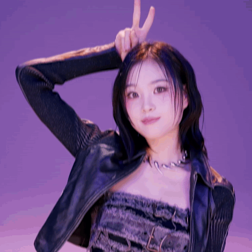 A Woman Wearing A Leather Jacket And A Necklace Is Making A Peace Sign GIF