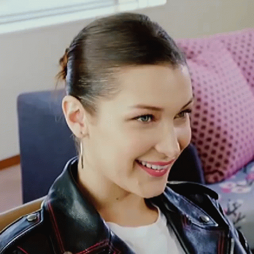 A Woman Wearing A Leather Jacket And Earrings Is Smiling GIF