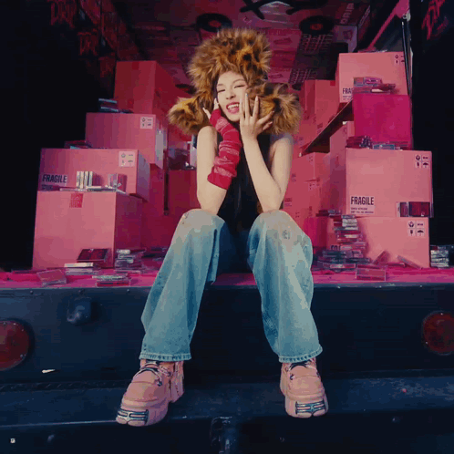 A Woman Wearing A Leopard Print Hat Sits In Front Of Fragile Boxes GIF