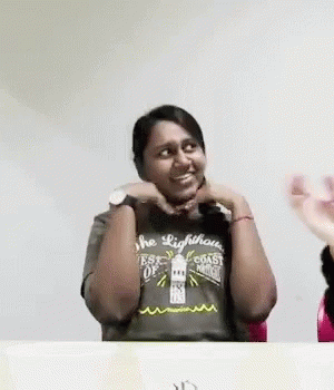 A Woman Wearing A Lighthouse T-Shirt Is Sitting At A Table With Her Hands On Her Face . GIF