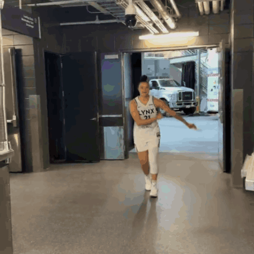A Woman Wearing A Lynx Jersey Is Walking Down A Hallway GIF